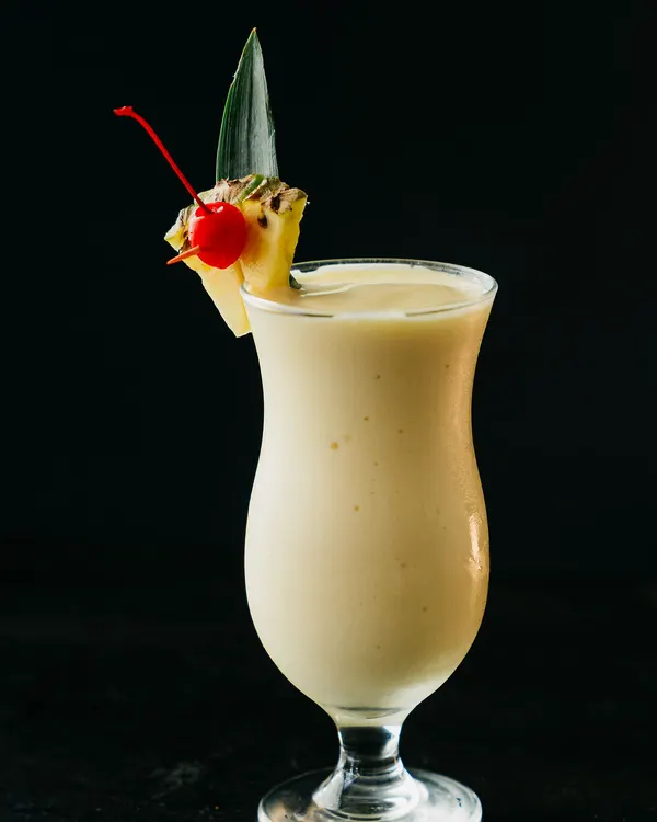 Bebida cremosa frozen en copa huracán, con un trozo de piña, una cereza y una hoja de piña.