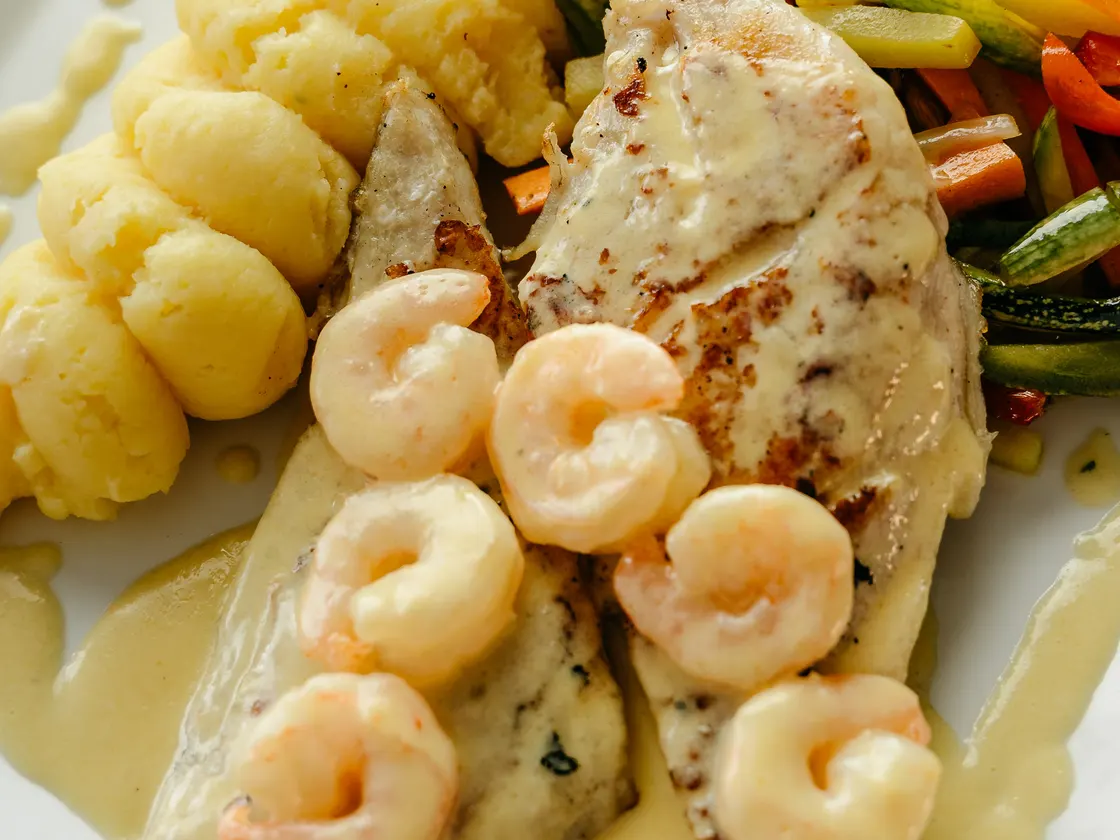 Filete a la plancha con camarones en salsa blanca, puré de papa y vegetales salteados.